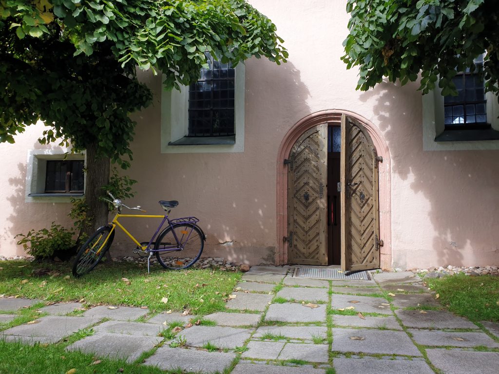 Ein gelb-violettes Fahrrad steht vor der leicht geöffneten Kirchentür in Kohlberg